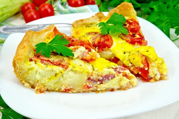 Torta de dois pedaços de abobrinha com tomate e ovos em um prato branco em um guardanapo, salsa em um fundo de tábuas de madeira