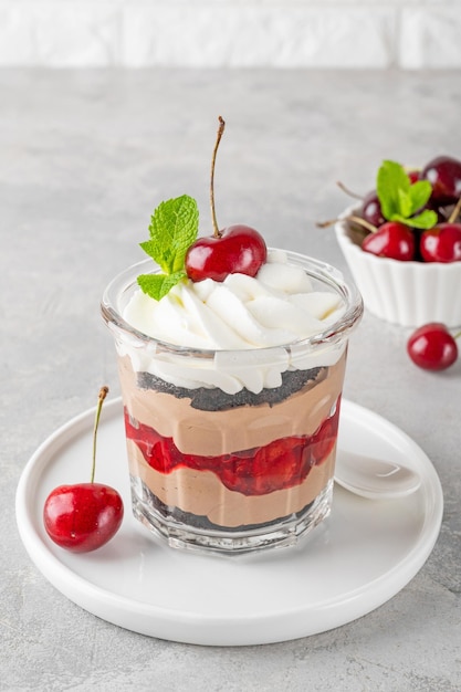 Torta de floresta preta de sobremesa em um copo de chocolate com biscoito de creme de chocolate e cereja em um fundo de concreto cinza