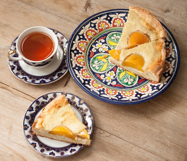Foto torta de frutas e pêssego em um pires brilhante com uma xícara de chá no fundo da mesa de madeira