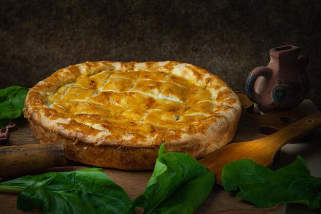 Torta de legumes caseira com espinafre e cebola em um fundo escuro de madeira