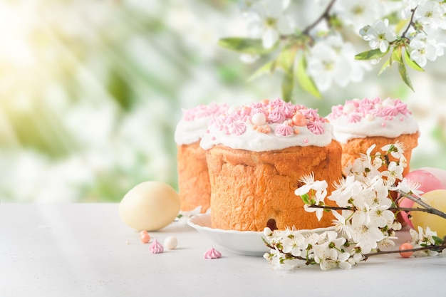 Torta de Páscoa tradicional com merengue suíço branco e decoração doce rosa e ovos pintados coloridos em fundo, cereja em flor ou jardim de maçãs inundado com luz solar e raios com espaço de cópia