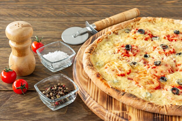 Torta de pizza quente cozida com calabresa, tomate, azeitonas pretas e mussarela na placa de madeira.