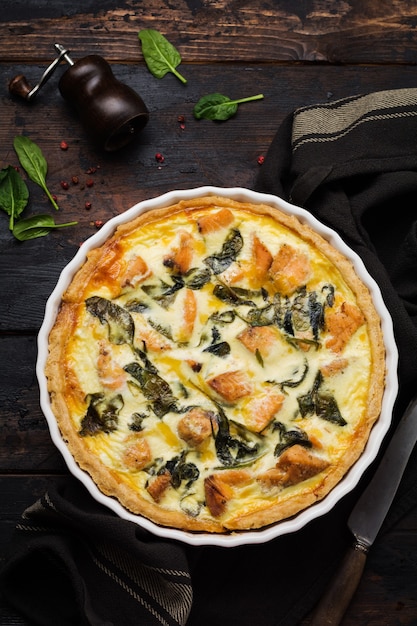 Torta de quiche caseira com peixe vermelho e espinafre em superfície de madeira escura