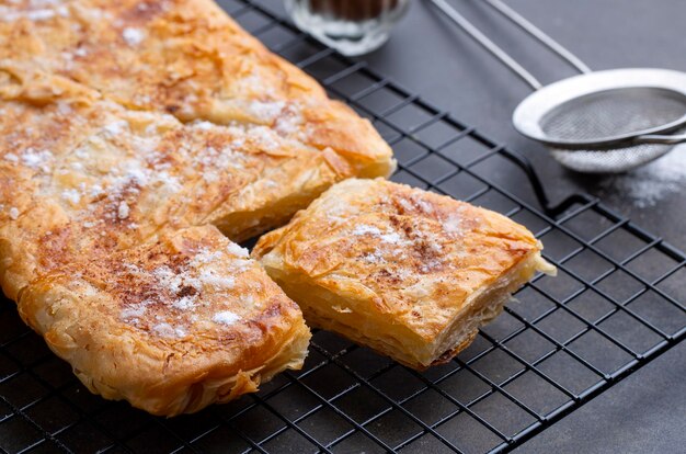 Foto torta grega chamada bougatsa com queijo, seção transversal ligeiramente desfocada e foco seletivo em açúcar em pó e canela