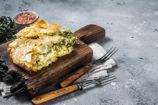 Torta grega Spanakopita com espinafre e queijo na placa de madeira Fundo cinza Vista superior Copiar espaço