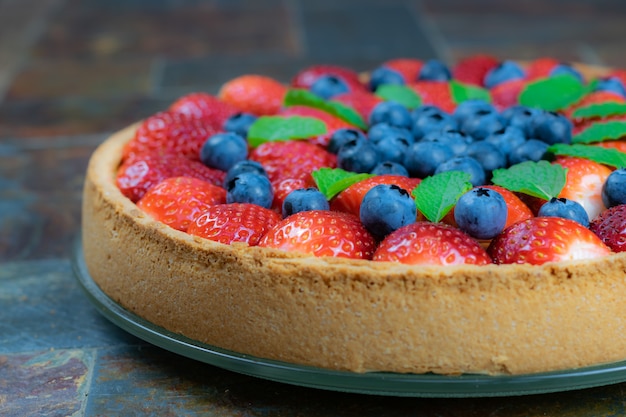 Foto torta hecha en casa con las fresas y los arándanos en una tabla de piedra.