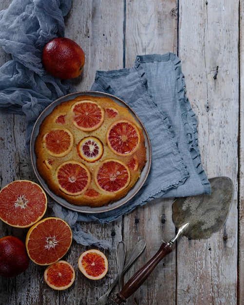 Torta hecha en casa con las naranjas de sangre en la tabla de madera ligera. Espátula pastel vintage