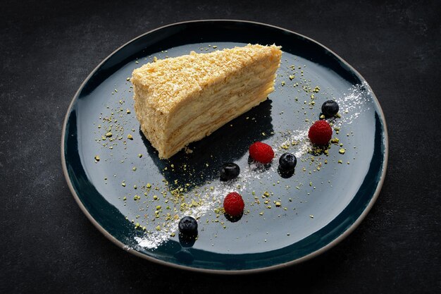 Torta de Napoleón en un plato oscuro con bayas en hormigón oscuro