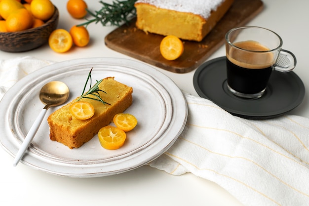 Torta de naranja servida, tabla de cortar de madera, kumquats frescos, café espresso