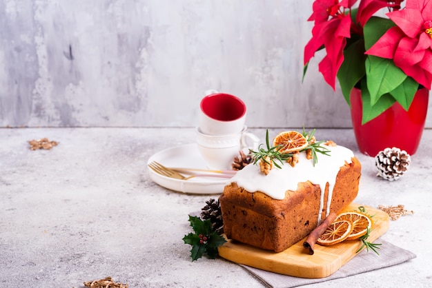 Torta de pan de fruta espolvoreada con glaseado, nueces y naranja seca sobre piedra. Pastel casero de Navidad e Invierno