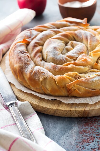 Torta redonda de burek com uma maçã em um fundo escuro. Cozinha tradicional sérvia. Foco seletivo. Vista do topo.