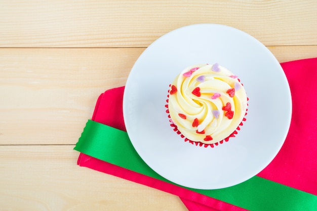 Torta roja de la taza del terciopelo en servilleta roja con la cinta verde sobre fondo de madera