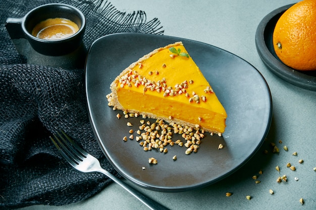 Torta vegetariana de cenoura e laranja em uma placa preta com uma xícara de café. Mesa cinza. Sobremesas saudáveis, sem açúcar