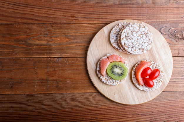 Tortas de arroz con salmón, kiwi y tomates cherry sobre fondo de madera.