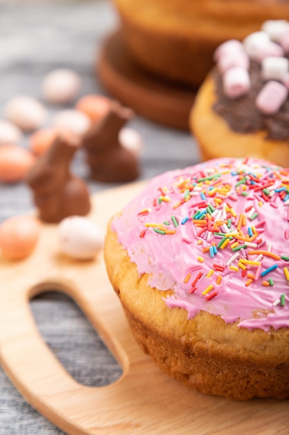 Tortas de Páscoa vitrificadas e decoradas caseiras com ovos de chocolate e coelhos em um fundo cinza de madeira e têxteis de linho.