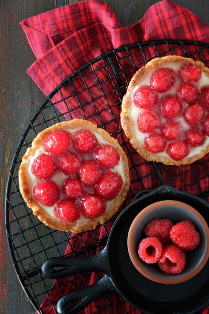 Tortas de shortbread de framboesa vermelha com creme de baunilha e framboesas frescas vitrificadas no rack de refrigeração em madeira marrom escura