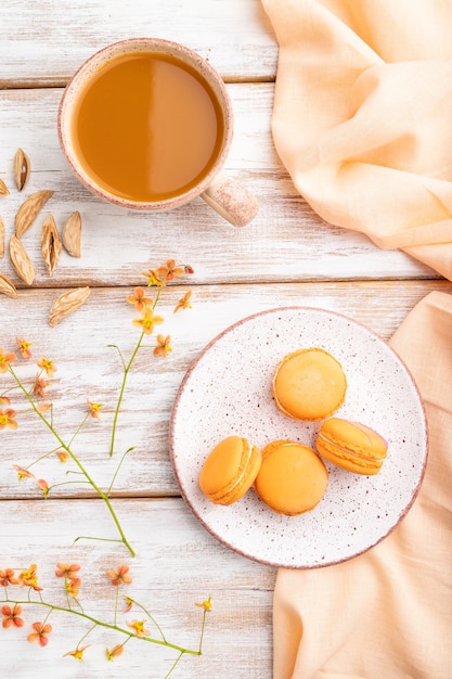 Tortas de macarons o macarrones de naranja con una taza de jugo de albaricoque en una madera blanca