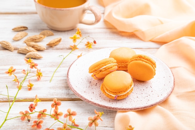 Tortas de macarons o macarrones de naranja con una taza de jugo de albaricoque en una madera blanca