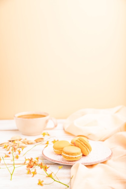 Tortas de macarons o macarrones de naranja con una taza de jugo de albaricoque sobre un fondo de madera blanca y textil de lino naranja.