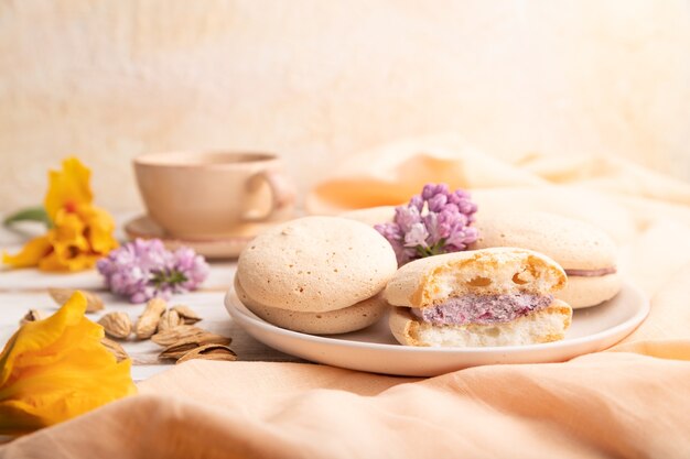 Tortas de merengues con taza de café sobre un fondo de madera blanca y textil de lino naranja. Vista lateral, de cerca,