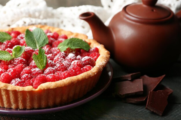 Torte mit frischen Himbeeren und Teekanne auf Holzhintergrund