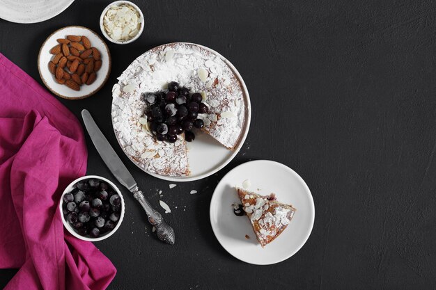 Torte mit gefrorenen Beeren und Mandeln auf dunklem Hintergrund und ein Stück fast Draufsichtkopierraum