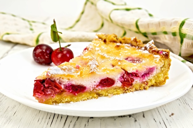 Torte mit Kirschen und Sauerrahm in einer Schüssel, Handtuch auf einem Hintergrund von Holzbrettern