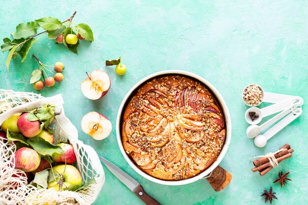 Torte mit Äpfeln und Zutaten auf einem grünen Steinhintergrund. Draufsicht.