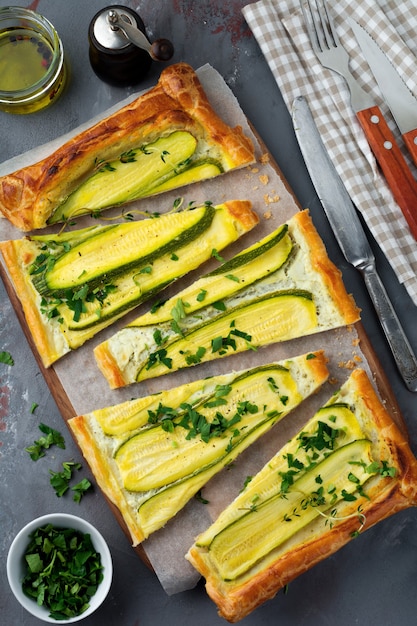 Torte mit Zucchini, Ricotta-Käse und Petersilie auf einem dunklen Betonhintergrund.