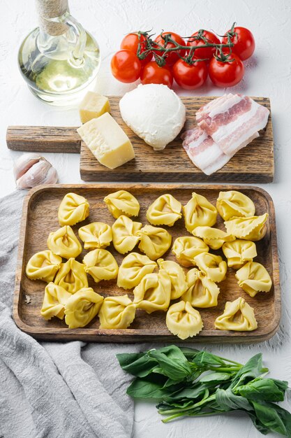 Tortellini caseiro italiano com ingredientes, presunto, manjericão, pesto, conjunto de mussarela, em bandeja de madeira, sobre fundo branco