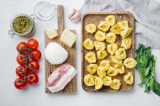 Tortellini caseiro italiano com ingredientes, presunto, manjericão, pesto, conjunto de mussarela, em bandeja de madeira, vista de cima plana lay