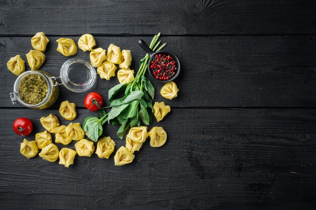 Tortellini cru com pesto de manjericão e pinho, no fundo da mesa de madeira preta, vista de cima plana, com espaço de cópia para o texto