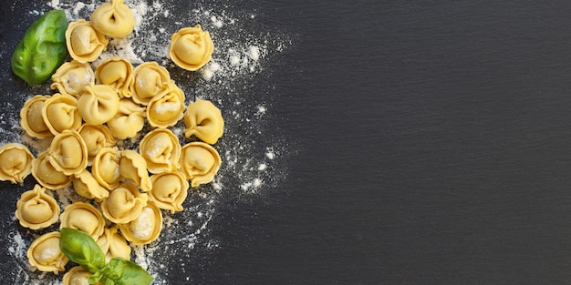 Tortellini italiano cru caseiro e manjericão em um fundo escuro