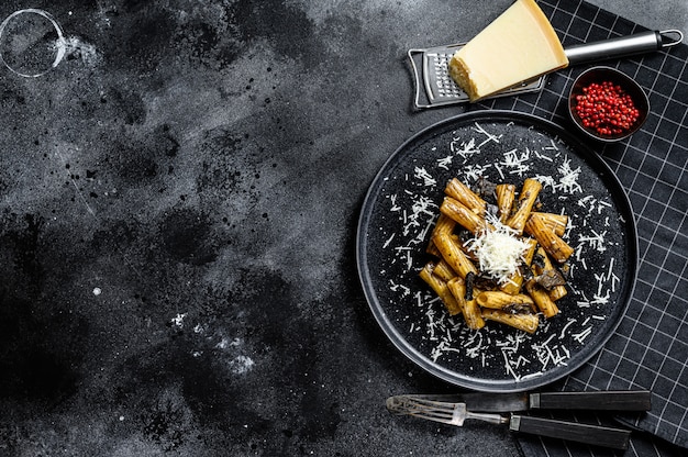 Tortiglioni de pasta con trufa negra, champiñones blancos, salsa de crema y queso parmesano. Fondo negro. Vista superior. Espacio para texto