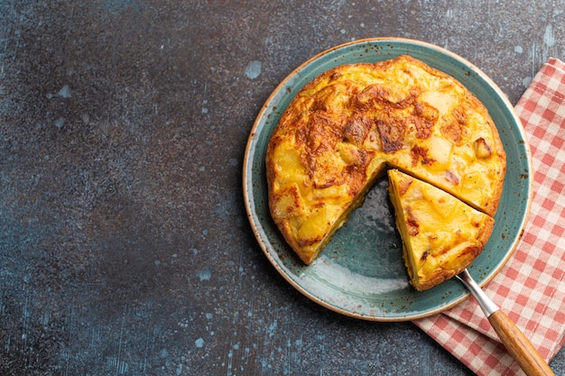 Tortilha espanhola caseira com corte de uma fatia - omelete com batatas no prato na vista superior de fundo rústico de pedra. Prato tradicional da Espanha Tortilla de patatas para almoço ou lanche, espaço para texto