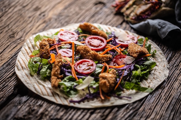 Tortilla abierta con nuggets de pollo, tomates cherry, col lombarda, ensalada y tiras de zanahoria.