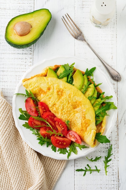 Tortilla con aguacate, tomate y rúcula en placa de cerámica blanca sobre superficie de piedra clara