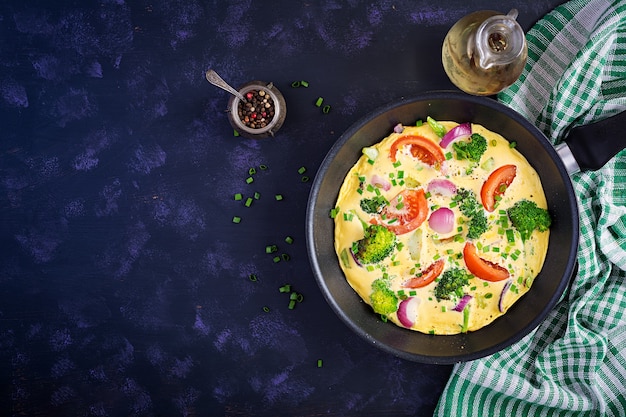 Tortilla con brócoli, tomates y cebollas rojas en una sartén de hierro. Frittata italiana con verduras. Vista superior, arriba