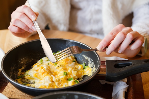 Tortilla caliente con verduras en una sartén, mano femenina con tenedor y cuchillo almuerza