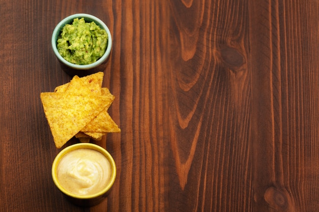 Foto tortilla chips nachos, sauce guacamole und käsesauce auf holzhintergrund. platz für text