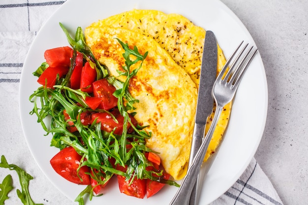 Tortilla clásica con queso y ensalada de los tomates en la placa blanca, visión superior.