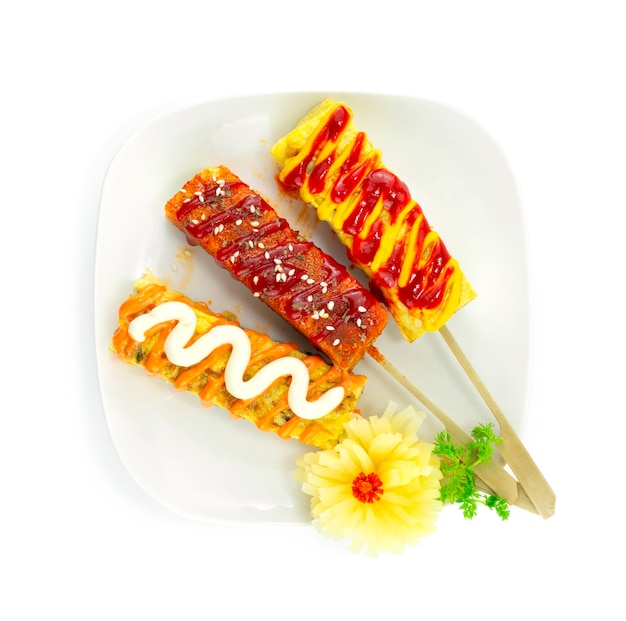 Tortilla coreana de huevos enrollados en estilo pinchos. Deliciosa tortilla Gyeran Mari hecha de capa de huevos cubierta con salsa picante, mayonesa y salsa de natillas decorada con rábano picado tallado topview