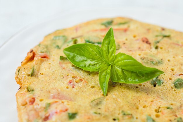 Tortilla de desayuno con pimiento rojo y cebolletas verdes servidas con hojas de albahaca Comida de desayuno de estilo italiano en un plato blanco Vista superior enfoque selectivo