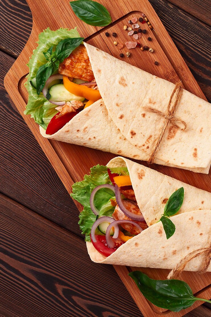 Tortilla embrulhando frango mexicano grelhado com burritos de vegetais em uma mesa de madeira sem pessoas
