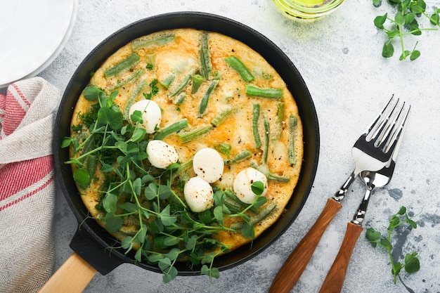 Tortilla con espinacas, judías verdes, patatas y espinacas, alimentos saludables en sartén negra sobre fondo rústico antiguo de piedra gris Frittata tradicional para el desayuno Tortilla de huevos Vista superior endecha plana Espacio de copia