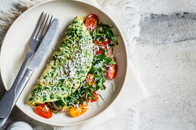 Foto tortilla de espinacas verdes con queso, rúcula y tomates en plato blanco, vista superior.