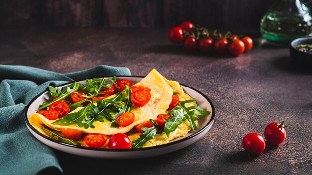 Tortilla francesa llena de tomates cereza y rúcula en un plato en la mesa