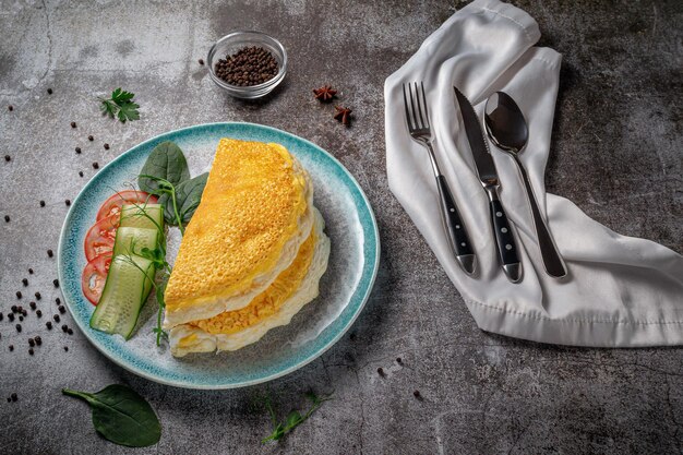 Tortilla con hierbas frescas y tomates en una placa azul con especias contra una mesa de piedra gris