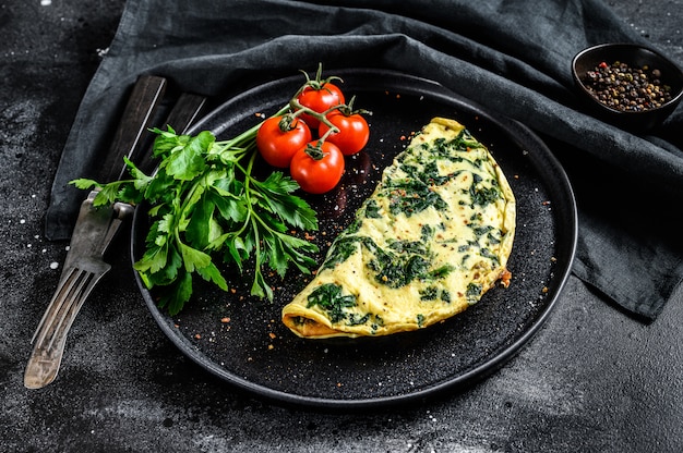 Tortilla de huevo con espinacas, servido en un plato con tomates. Superficie negra. Vista superior