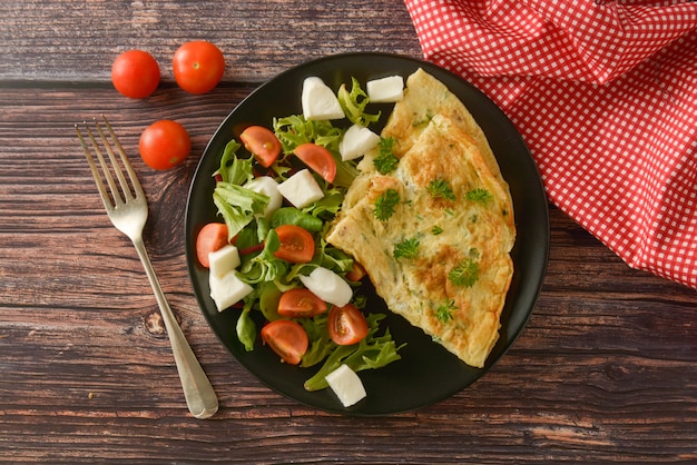 Tortilla de huevo con tomate cherry, mozzarella y ensalada verde. Mesa de madera con espacio de copia.